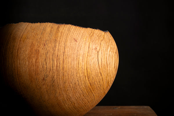 A close-up of a turned wooden bowl with a prominent wavy grain pattern, set against a solid black background.