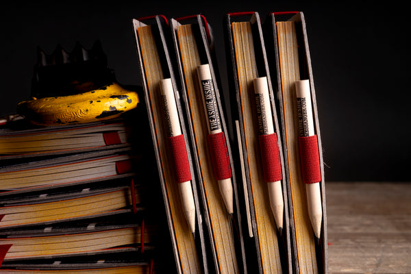 Four wooden pencils with red fabric loops and black printed text reading 'TREASURE inside' tucked inside the spines of diaries.