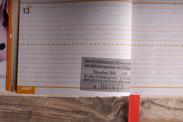 An open planner or notebook page with lined writing space, showing a January layout, orange dashed horizontal lines, and a small printed label on the page.