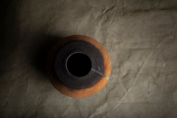 A round hollow form hand turned on the lathe from red oak with a dark center and a warm brown outer rim, photographed from above on a wrinkled taupe paper background.