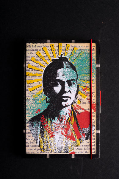 A hardcover journal featuring a vibrant pop-art style portrait of a woman, printed over a background of vintage book pages. The notebook has a red elastic closure band, photographed against a solid black background.
