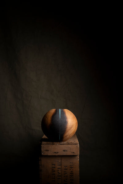 A spherical wooden object with a natural wood grain sits on top of a rustic wooden crate against a dark, textured background.