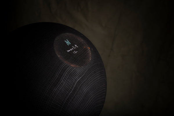 A close-up of a black hollow vessel turned from red oak with a visible signature and exposed wood grain. 