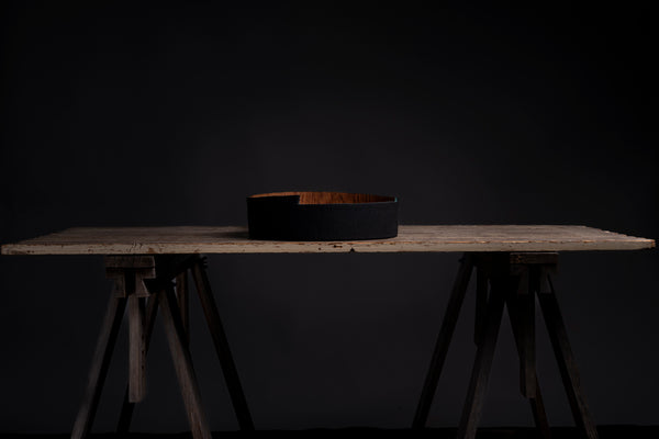 A black wooden bowl hand turned from red oak, displayed on a rustic wooden table against a dark background.