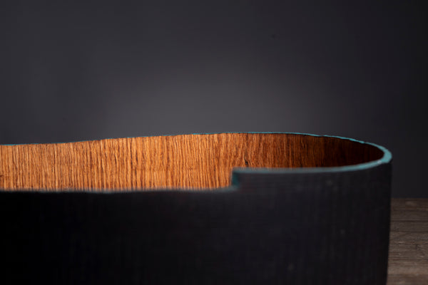 Close-up of a curved wooden bowl with a dark charred exterior and a warm brown wood grain interior, set against a dark studio background.