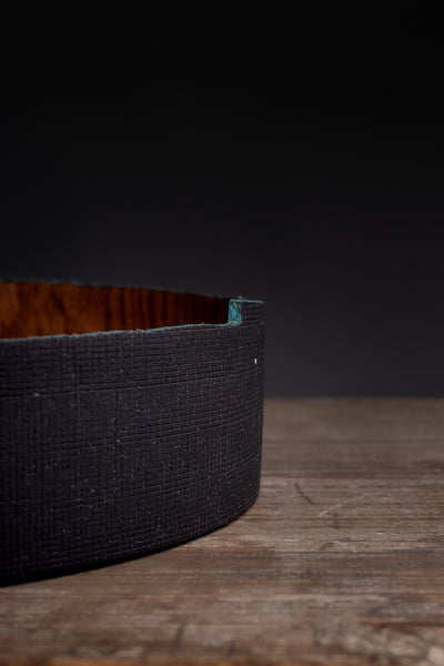 A close-up of a dark wall of a wooden bowl from red oak made by maalstrom studio resting on a rustic wooden surface against a dark background.