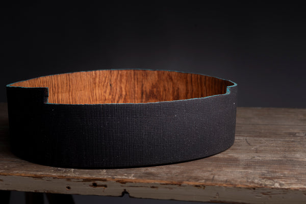 A handmade shallow wooden bowl made made from a natural red oak, resting on a rustic wooden table against a dark background.