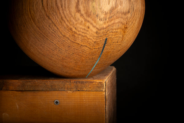 A close-up of a round wooden object with prominent wood grain resting on a wooden block against a solid black background.