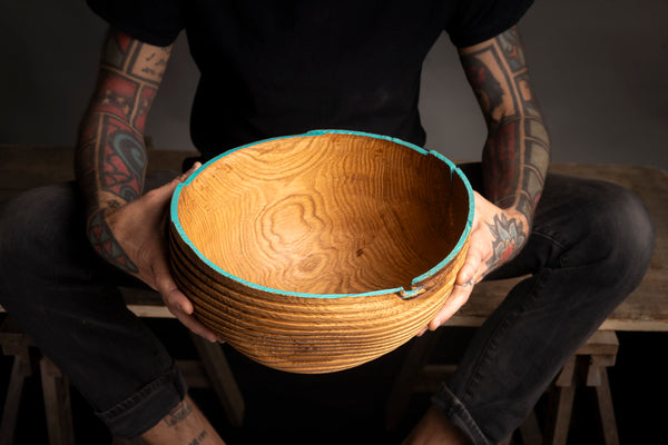 Person holding a wooden bowl with visible tattoos on arms