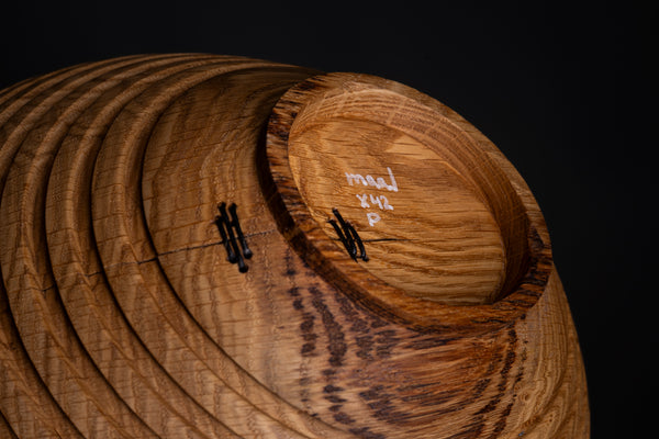 Sculptural stitched oak bowl photographed on a dark background