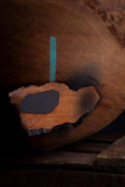 A close-up of a carved wooden bowl with a prominent natural wood slice inlay showing detailed grain patterns, set against a dark, rustic background.