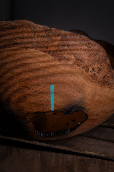 A close-up of a large, rustic wooden bowl  with a live edge showing detailed wood grain, set against a dark background.