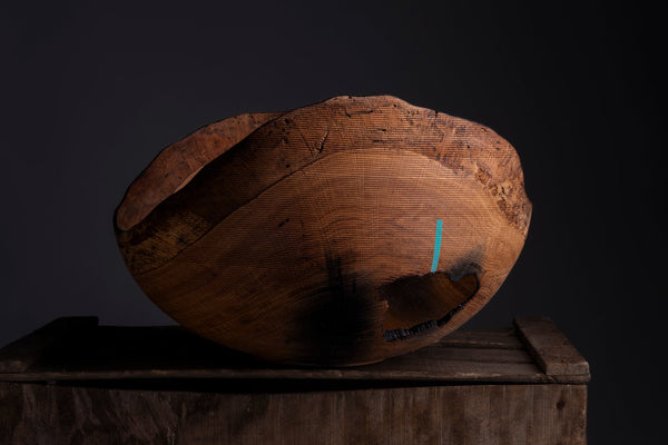 A turned wooden bowl from aok with a natural irregular shape and visible wood grain, displayed on top of rustic wooden crates against a dark studio background.