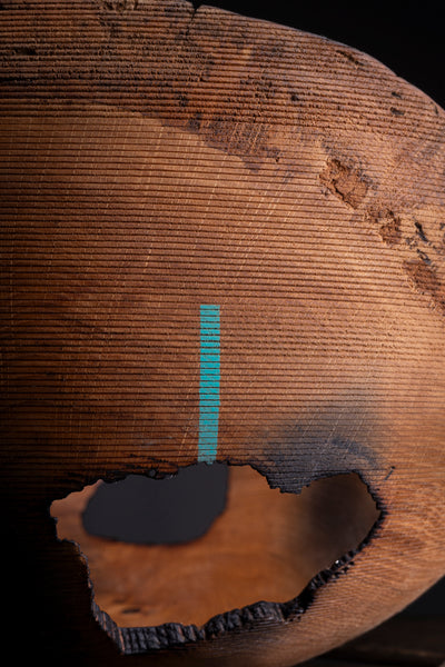 A close-up of a hand turned wooden bowl from oak  with a rough cutout opening, showing detailed wood grain and a small vertical turquoise stripe against a dark background.