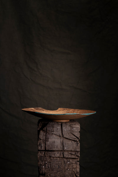 Thin wooden oak bowl on a wooden pedestal against a dark background
