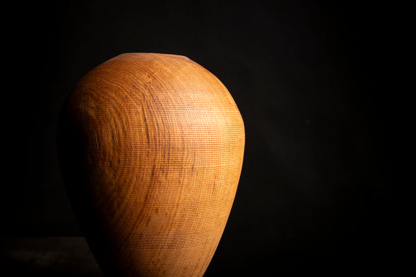 A teardrop-shaped wooden vase with a textured, basketweave-like wood grain pattern, shown against a solid black background.