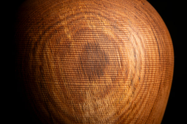 Close-up of a round wooden object with a prominent circular wood grain pattern, set against a solid black background.