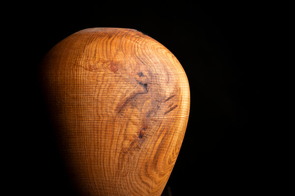 A close-up of a textured wooden object with a rounded, bulbous shape and prominent natural wood grain, set against a solid black background. Turned on the lathe from red oak.